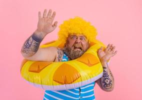 Fat afraid man with wig in head is ready to swim with a donut lifesaver photo