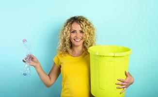 Woman is ready to puts a plastic bottle in the garbage can. cyan background photo