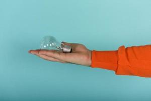 Man holds a lightbulb in hand. concept of creativity and solution. cyan background photo