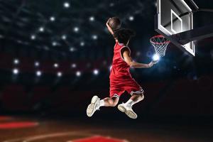 Basketball player in red uniform jumping high to make a slam dunk to the basket photo