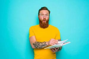 hombre con amarillo camiseta y barba es sorprendido acerca de alguna cosa foto