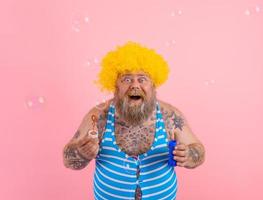 Amazed man with yellow wig in head play with bubbles soap photo