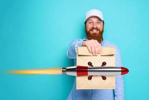 Deliveryman with wondered expression ready to deliver fast bag with food like a rocket. cyan background. photo