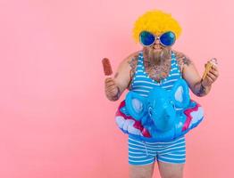 Fat man with beard and wig eats a popsicle and an icecream photo