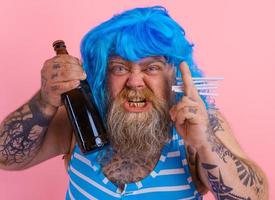 Fat man with beard and wig smokes cigarettes and drinks beer photo