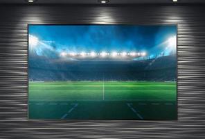 acecho un fútbol evento en un grande televisión pared montado y iluminado por focos foto