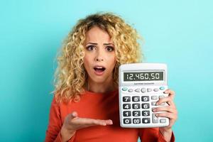 Girl is shocked and shows her debt on calculator display. Cyan background photo