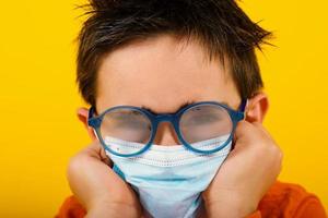 Child with fogged lens due to face mask for covid-19 coronavirus. yellow background photo