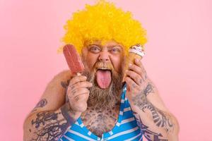 Fat man with beard and wig eats a popsicle and an icecream photo