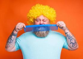 Fat doubter man with beard, tattoos and sunglasses combs himself with a giant comb photo