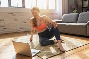 Young woman follows with a laptop a gym exercises. She is at home due to coronavirus codiv-19 quarantine photo
