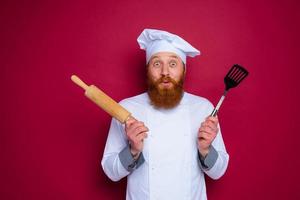 happy chef with beard and red apron chef holds wooden rolling pin photo