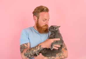 hombre con barba y tatuajes caricias un gris gato foto