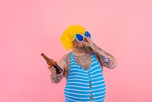 Fat man with beard and wig smokes cigarettes and drinks beer photo