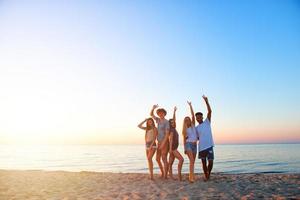 grupo de contento amigos teniendo divertido a Oceano playa a amanecer foto