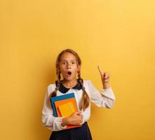 Young student is with shocked expression and indicates something. Yellow background photo