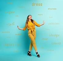 Brunette girl with a yellow clothes walks over a cyan background. Concept of fashion and shopping with joyful expression photo