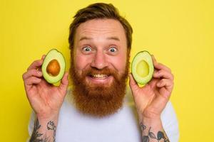 Happy man with beard and tattoos holds an avocado photo