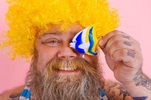 Fat happy man with beard and sunglasses have fun with a fish toy photo