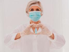 Doctor with mask makes a heart with her hands and covid-19 vaccine photo