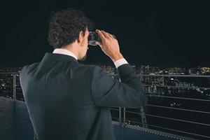 Businessman looks at the city with binoculars during night. Future and new business opportunity concept photo