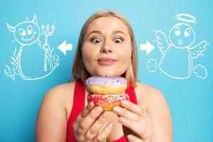 Fat girl thinks to eat donuts instead of does gym. Concept of indecision and doubt with angel and devil suggestion photo