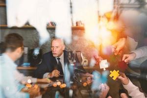 Business people join puzzle pieces in office. Concept of teamwork and partnership. double exposure with light effects photo