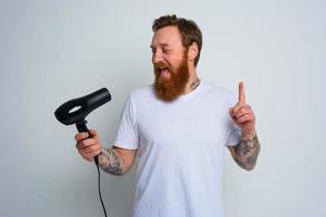 Happy man with beard use hair dryer as microphone and dances photo