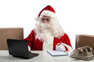Papa Noel claus trabajos en oficina con ordenador portátil y teléfono foto