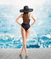 mujer en elegante negro sombrero y traje de baño mira a mar foto