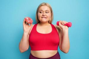 grasa niña piensa a comer rosquillas en lugar de lo hace gimnasia. concepto de indecisión y duda foto