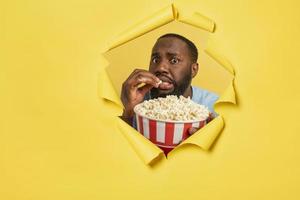 Worried boy watches a horror film behind a hole. concept of entertainment and streaming tv. yellow background photo