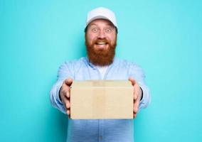 Courier is happy to deliver a carton box. Emotional expression. Cyan background photo