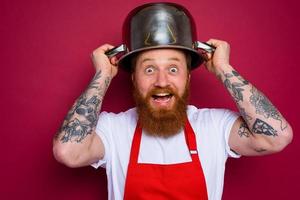 Happy chef with beard and red apron plays with pot photo