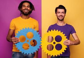 Friends with gears in hand over yellow and violet background. Concept of integration, union and partnership photo