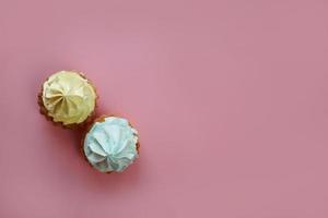 un parte superior ver de dos capcakes con amarillo y azul crema estar en un rosado antecedentes. aislado. rosado antecedentes. Copiar espacio foto