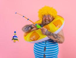 Fat happy man with wig in head plays with the fishing rod photo