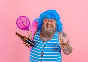 Fat man with beard and wig smokes cigarettes and drinks beer photo