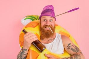 contento hombre es Listo a nadar con un rosquilla salvador de la vida con cerveza y cigarrillo foto