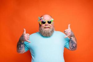 Fat happy man with beard, tattoos and sunglasses is ready for the summer photo