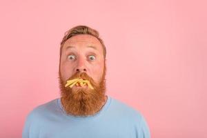 Hungry man with beard and tattoos eats a sandwitch with hamburger and potatoes photo