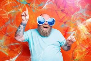 Fat happy man with beard, tattoos and sunglasses dances music photo