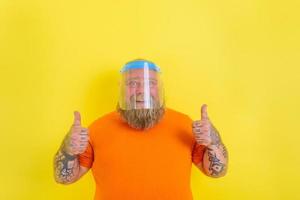Happy man with beard and tattoos wears a protective face shield against covid-19 photo