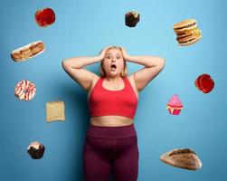 Fat girl in fitness suite wants to start a diet but has doubts about the food to buy. Cyan background photo