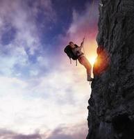 hombre sube un alto peligro montaña con un cuerda durante puesta de sol foto