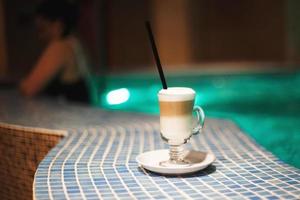 a cup of coffee in the pool and a girl in the background photo