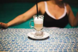 a cup of coffee in the pool and a girl in the background photo