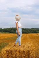 girl in straw hat stands on a haystack on a bale in the agricultural field after harvesting photo