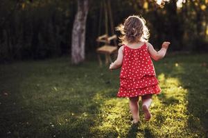 pequeño niña corriendo a puesta de sol mediante el césped foto