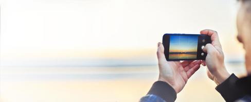 un hombre tomando un foto de el hermosa puesta de sol en su teléfono